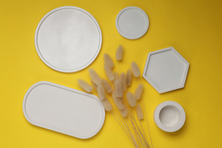 Set of decorative white plaster trays of different shapes on yellow background with dry flowers. Stands for candles or jewelry. Top viewの写真素材