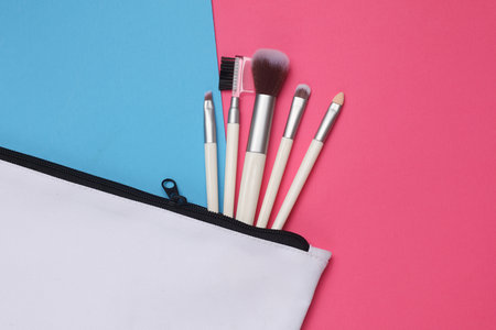 white fabric cosmetic bag with makeup brushes on pink blue background. Mockup for design
