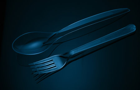 Transparent plastic fork and spoon on a black background in blue lightの写真素材