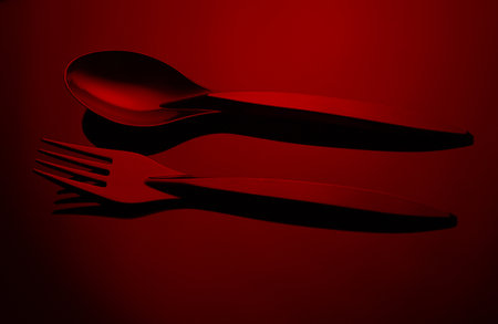 Black plastic spoon and fork in red neon lightの写真素材