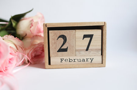 Wooden block calendar with the date February 27 and bouquet of roses on white background