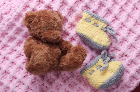 Knitted shoes for newborn and toy bear on a pink backgroundの写真素材