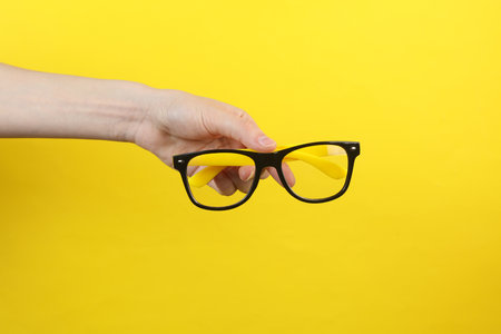Hand holding eyeglasses on yellow background