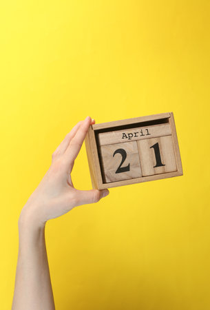 Wooden block calendar with date April 21 in hand on yellow backgroundの写真素材