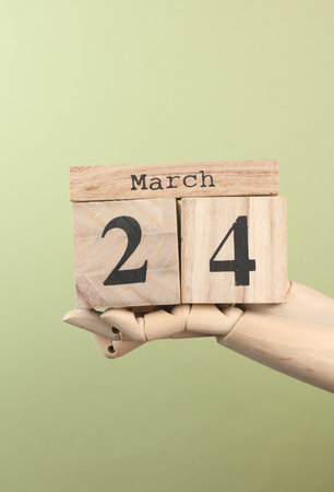 Wooden block calendar with date March 24 in the hand of puppet on green backgroundの写真素材