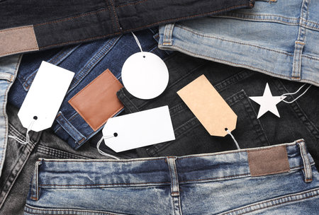 Assortment of many different fashionable jeans pants with blank paper tags. Shopping, sale concept