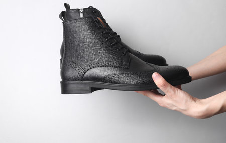 Hands holding black brogue boots on gray backgroundの写真素材