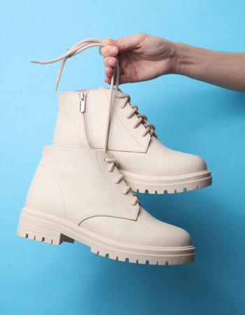 Woman's hand holds a white leather boots by the lace on blue backgroundの写真素材