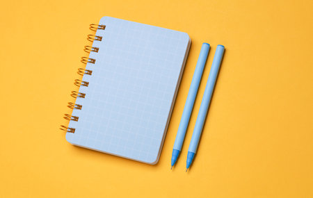 Notepad with pens on a yellow background. Top view