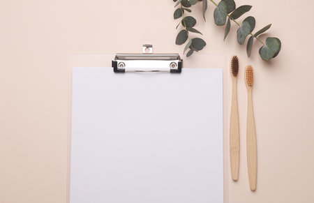 Eco bamboo toothbrushes with a clipboard and a sprig of eucalyptus on a beige background. Visit to the dentist, dental care. Flat layの写真素材