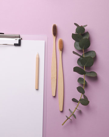 Eco bamboo toothbrushes with a clipboard and a sprig of eucalyptus on purple background. Dental care. Flat layの写真素材