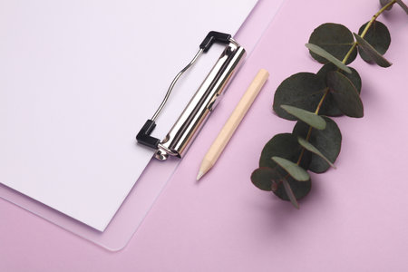 Clipboard with pencil and sprig of eucalyptus on purple background.の写真素材