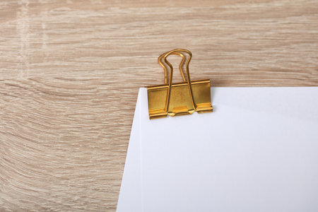 Golden clip with white empty sheet of paper on the table