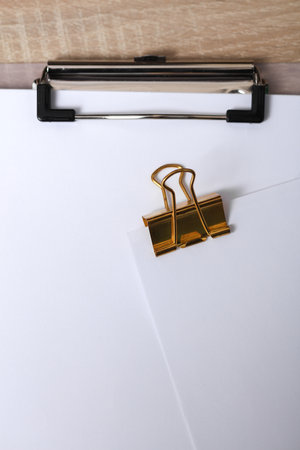 Golden clip with white empty sheet of paper on the table