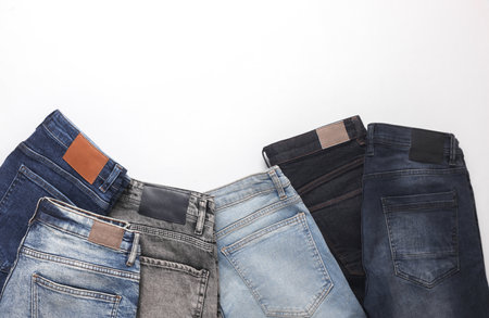 Assortment of many different fashionable jeans pants with leather tags on white backgroundの写真素材