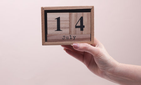 Female Hand holding wooden block calendar with the date July 14 on beige backgroundの写真素材