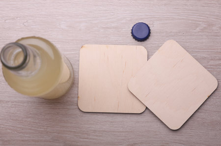 Wooden square drink coasters and bottle of beverage on the tableの写真素材