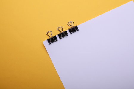 White sheet of paper with binders on yellow backgroundの写真素材