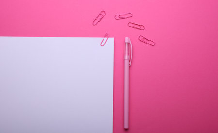 White sheet of paper with paper clips and pen on pink backgroundの写真素材