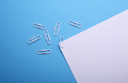 White sheet of paper with paper clips on blue background