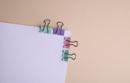 White sheet of paper with colored binders on beige background