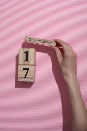 Hands holding wooden block calendar with date September 17 on pink backgroundの写真素材