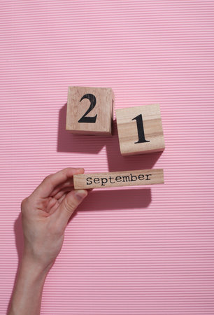 Hands holding wooden block calendar with date September 21 on pink background