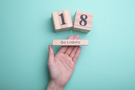 Hand holding wooden block calendar with date October 18 on mint green backgroundの写真素材