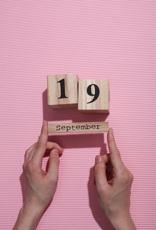 Hands holding wooden block calendar with date September 19 on pink backgroundの写真素材