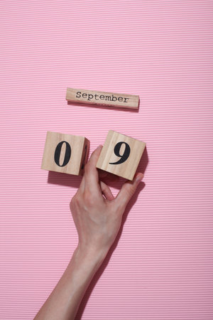 Hands holding wooden block calendar with date September 09 on pink backgroundの写真素材
