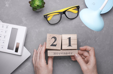 Hands holding a wooden block calendar 21 November against the background of a work space. Top view