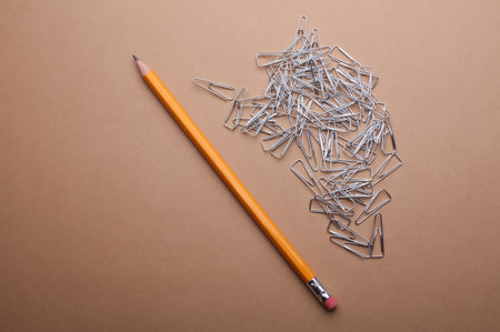 Metal paper clips and pencil on brown backgroundの写真素材