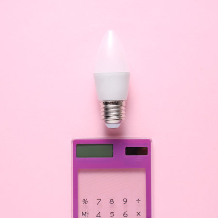 Calculator with energy-saving LED light bulb on a pink background. Creative idea, business concept