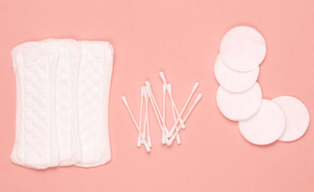 Hygiene products on coral color pastel background. Cotton pads, women's pads, cotton ear sticks. Top view, flat layの写真素材