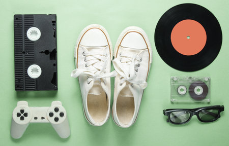 Old fashioned pop culture attributes from 80s on green color background. Old sneakers, gamepad, audio cassette, videotape, vinyl plates, 3d glasses. Minimalism, top viewの写真素材