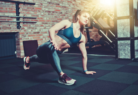 Athletic young woman with perfect body in sportswear does stretches for legs in gym. Warm up before trainingの写真素材
