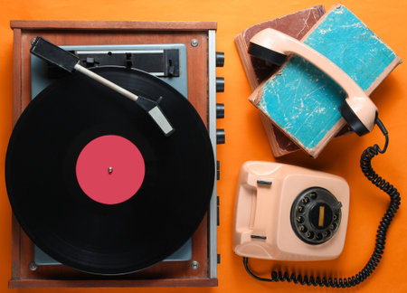 Old-fashioned objects on orange background. Retro style, 80s, pop culture. Top view. Vinyl player, rotary phone, old booksの写真素材