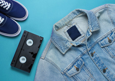Retro style stuff. Videotape, jeans jacket, sneakers on blue background. Top viewの写真素材