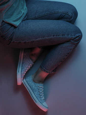 The concept relax. Women's legs in jeans and sneakers. Neon light. Top view.