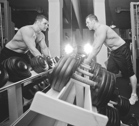 Athletic man with a naked torso takes dumbbells from the rack in the gymの写真素材