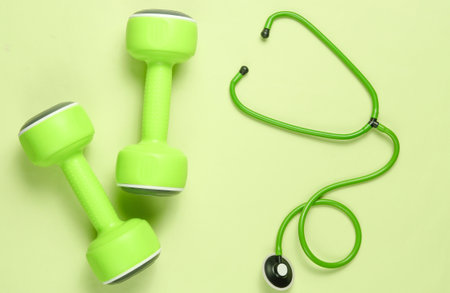 Healthy heart and strong muscles. Dumbbells and stethoscope on green background. Top view. Flat layの写真素材