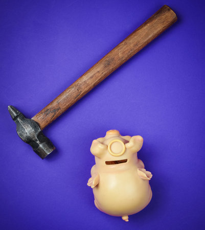 Piggy bank and hammer on purple background. Top view.の写真素材
