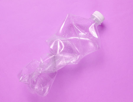 Minimalistic ecological concept. Crumpled plastic bottle on purple background. Environmental plastic...