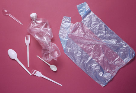 The concept of plastic pollution environment. Cellophane bag, plastic bottle, disposable forks and spoons, cocktail tubes on red background. Top viewの写真素材