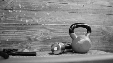 Functional training concept. Kettlebell, dumbbell, jump rope stand on a fitness step platform against the wooden wall background. Copy spaceの写真素材