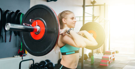 Smiling fit woman holding barbell with her hands and doing exercise for her muscles in the gym....