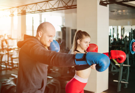 Couple exercising punching. Young woman and man training punches in boxing gloves at the gym.の写真素材