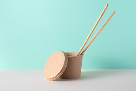 Eco cardboard round food box with chopsticks on table, turquoise background