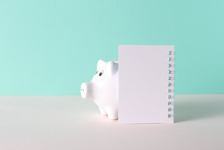 Piggy bank with empty white notebook on mint green backgroundの写真素材