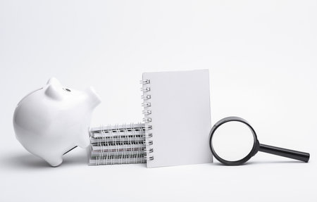 Notepads with piggy bank and magnifying glass on white backgroundの写真素材
